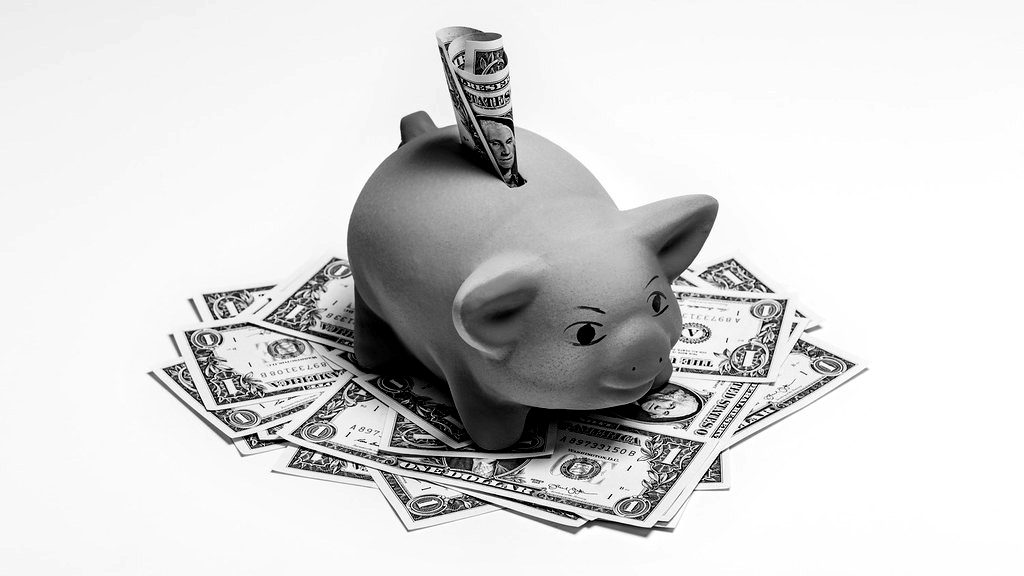 A red piggy bank on scattered dollar bills