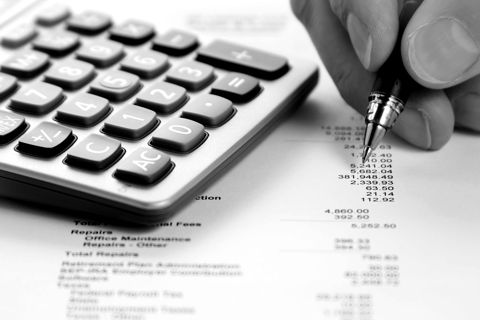 A hand with a pen beside a calculator and a printed statement