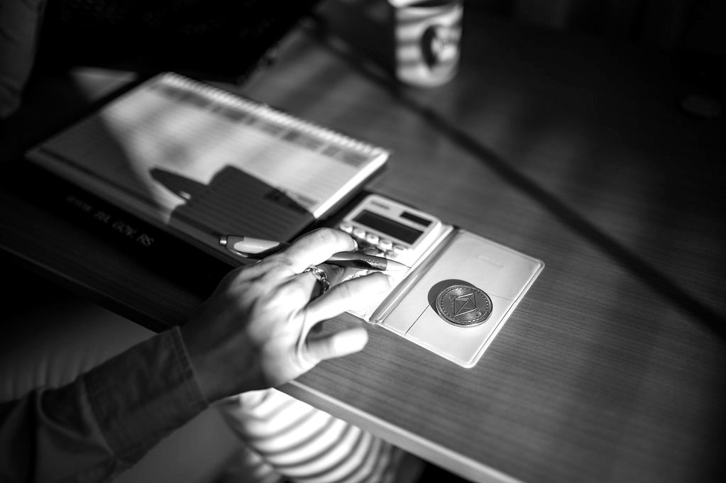 A hand using a calculator beside a coin and a phone