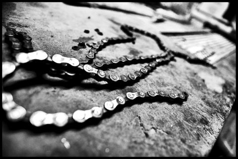 A broken bicycle chain lying on concrete, in black and white