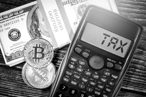 Gold-coloured Bitcoin tokens beside a calculator showing the word TAX and dollar bills