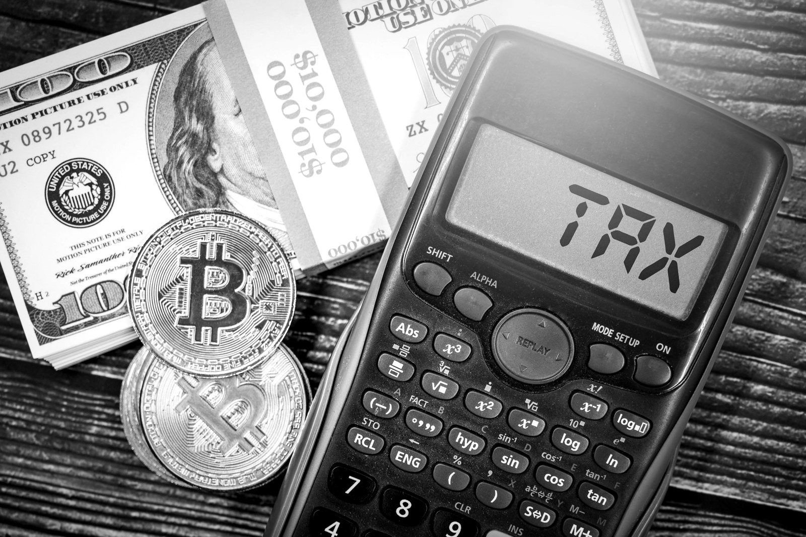 Gold-coloured Bitcoin tokens beside a calculator showing the word TAX and dollar bills