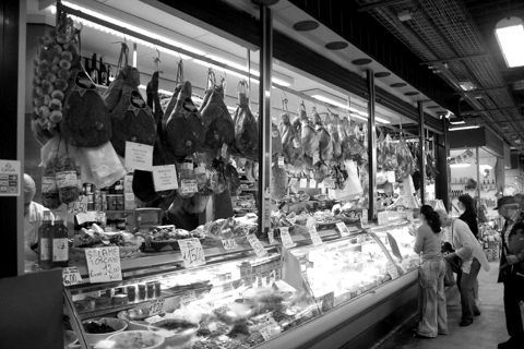A busy market food counter with hanging produce