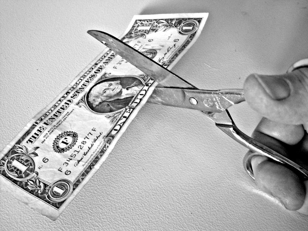 Scissors cutting a US one-dollar bill in half