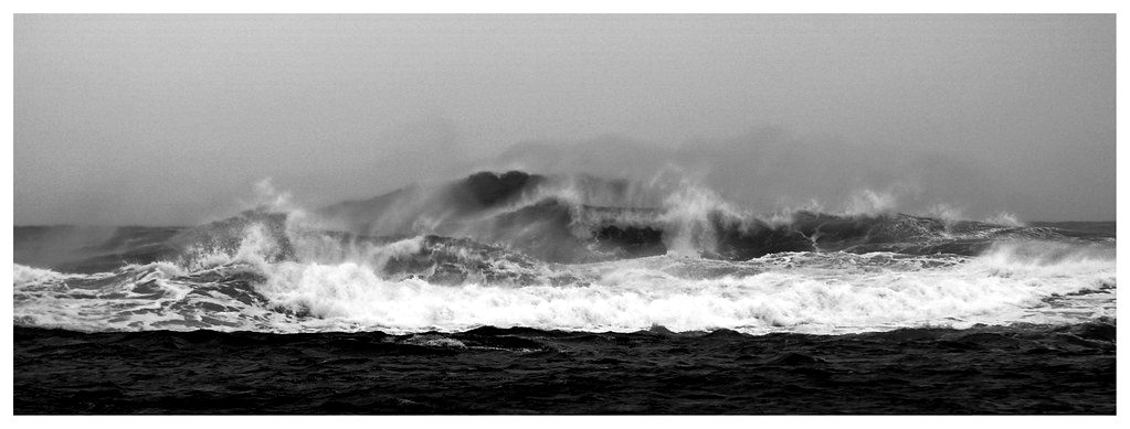Waves breaking against rocks under a grey sky